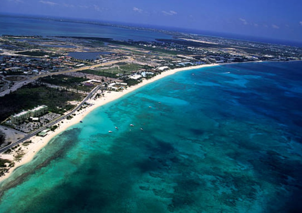 Aerial view of Grand Cayman island showing Seven Mile Beach, turquoise reef water, resorts and boats along the coastline