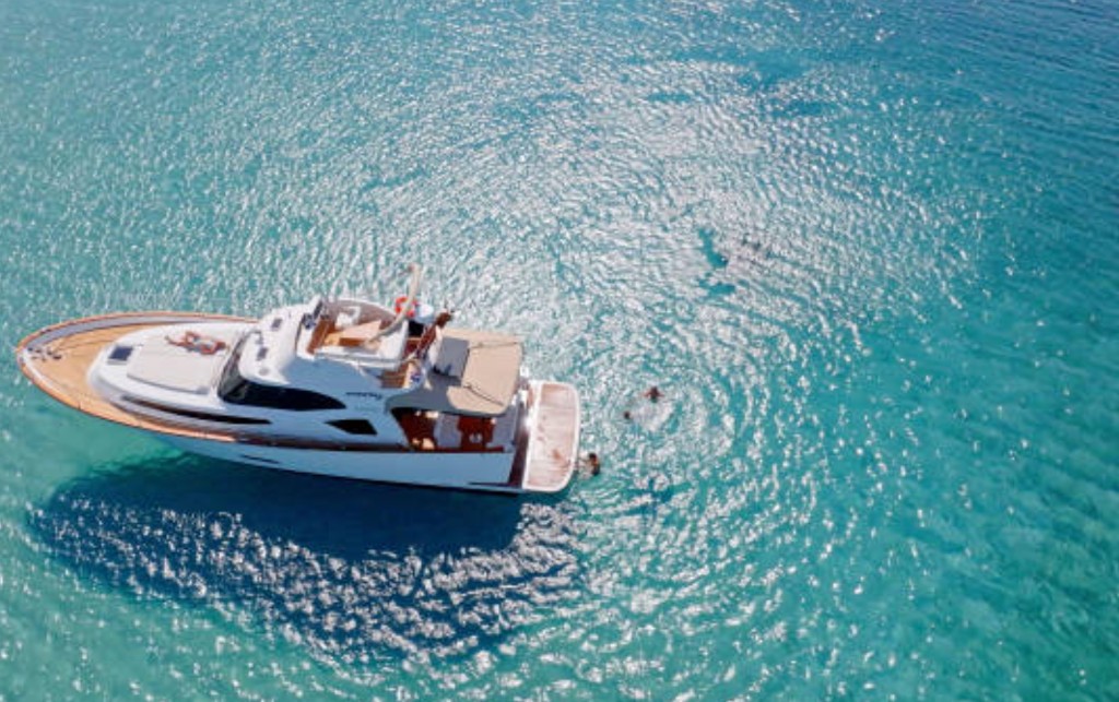 Aerial view of a private motor yacht in turquoise shallow water off Grand Cayman with guests swimming near stingrays on a custom charter tour